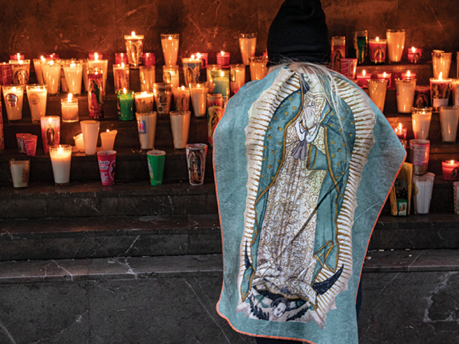 Woman prays before candles devoted to Our Lady of Guadalupe