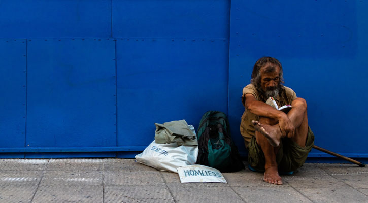 Homeless man sitting against blue wall