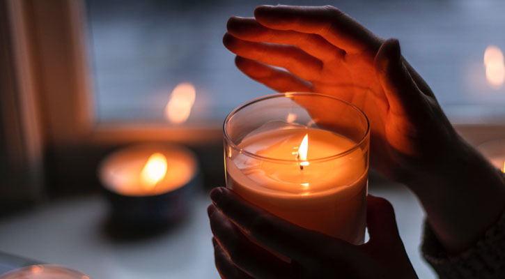 Hands holding lit jar candle